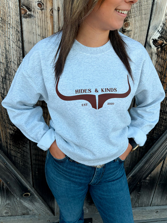Close-up of Hides & Kinds Original Logo Crewneck in ash grey with a brown longhorn logo across the chest, styled with blue jeans.