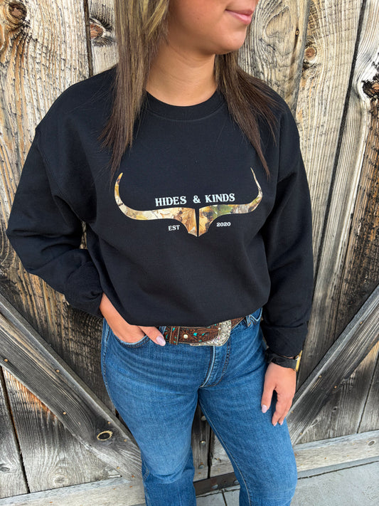 Close-up of Hides & Kinds Original Logo Crewneck in black with a camouflage longhorn graphic, styled with blue jeans and a western belt