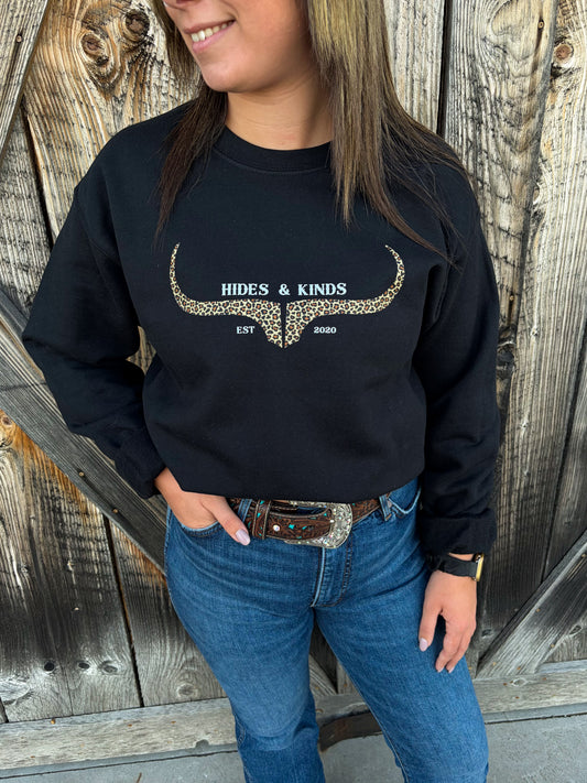 Close-up of Hides & Kinds Original Logo Crewneck in black with a leopard print longhorn logo, styled with blue jeans and a western belt.