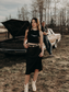 Woman wearing a black Hides & Kinds cropped high neck ribbed tank top with white western longhorn logo standing in front of a vintage car in a western inspired photoshoot.