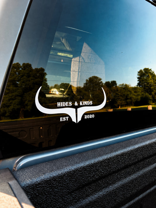 Close-up of the white Hides & Kinds Original Logo vinyl decal with longhorn horns, Hides & Kinds lettering and EST 2020 details on a pickup truck window