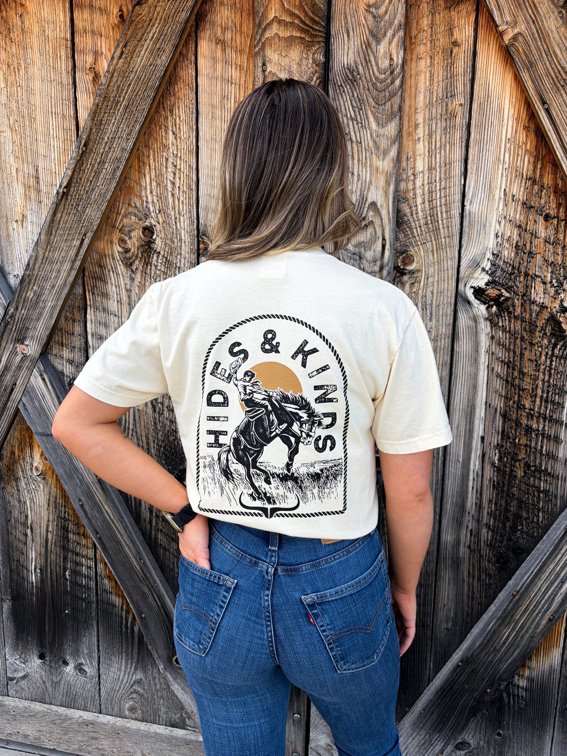 Full body view of Hides & Kinds Outlaw Rider Tee in ivory showing large western rider back print styled with jeans and boots