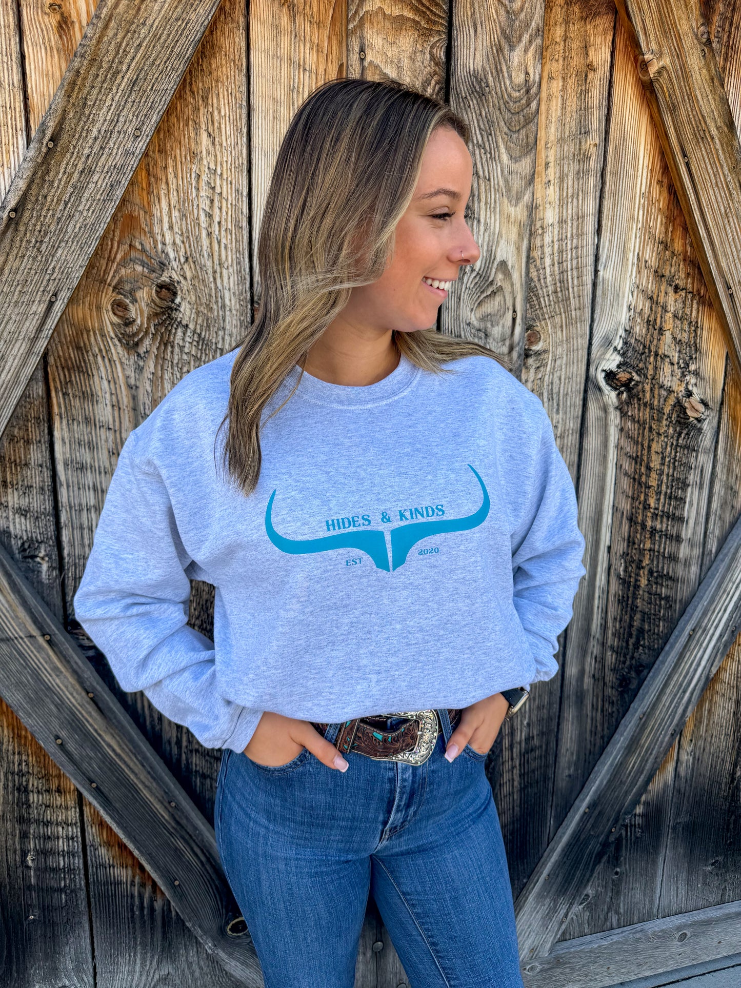 Western outfit featuring grey crewneck with teal logo and denim jeans