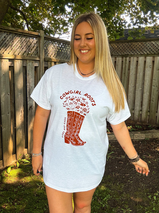 Woman wearing white Cowgirl Roots graphic tee by Hides and Kinds, styled as a dress with western accessories.