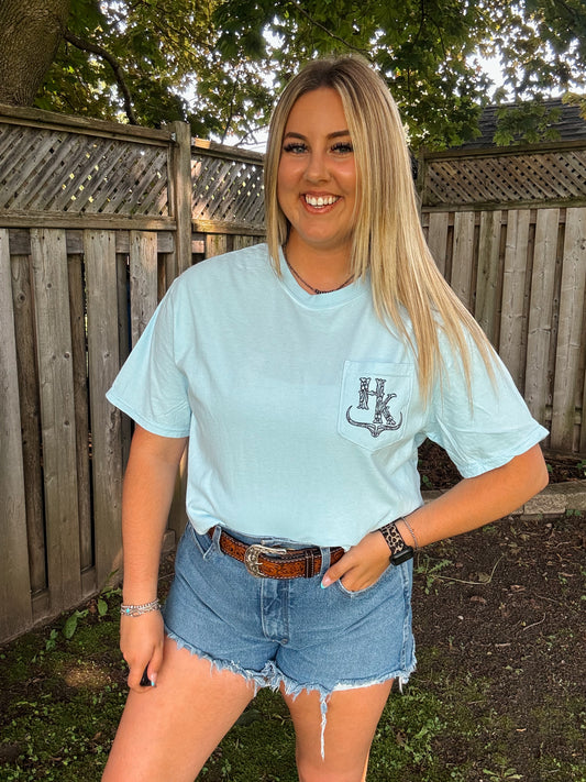 Woman wearing HK Branded Pocket Tee in chambray blue with stitched logo and casual western summer outfit.