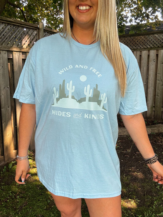 Close-up of light blue western tee with cactus and desert design and "Wild and Free" text by Hides and Kinds.