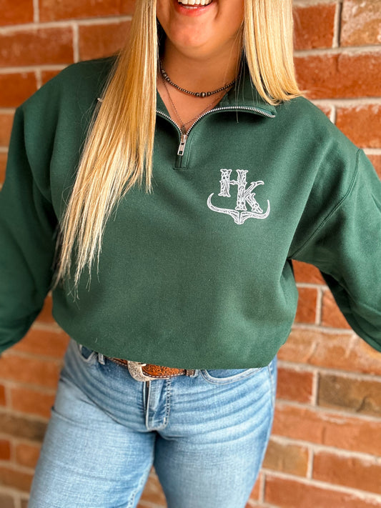 Close up of forest green quarter zip with HK bullhorn logo on left chest, worn with denim jeans and western belt.