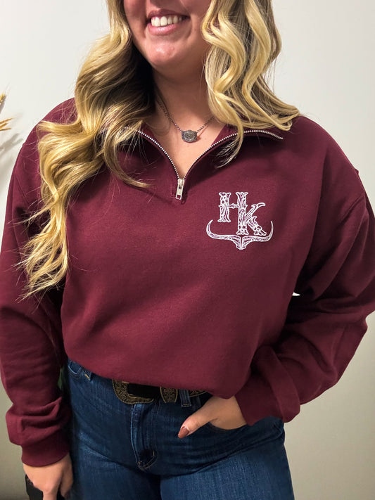 Close-up of HK maroon quarter zip with white western logo on front, styled with denim jeans.