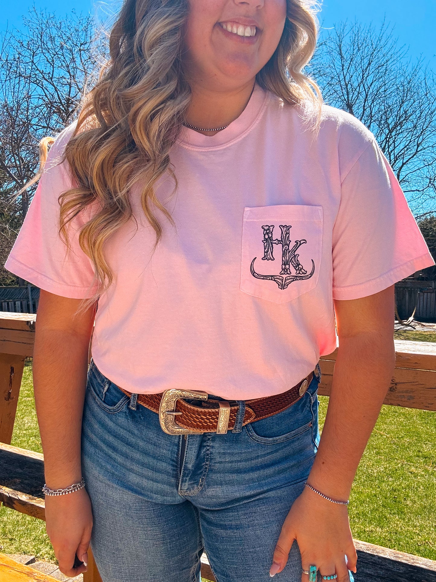 Modeled image of the Blossom Pink branded pocket tee styled with denim jeans and western accessories, highlighting the logo placement.