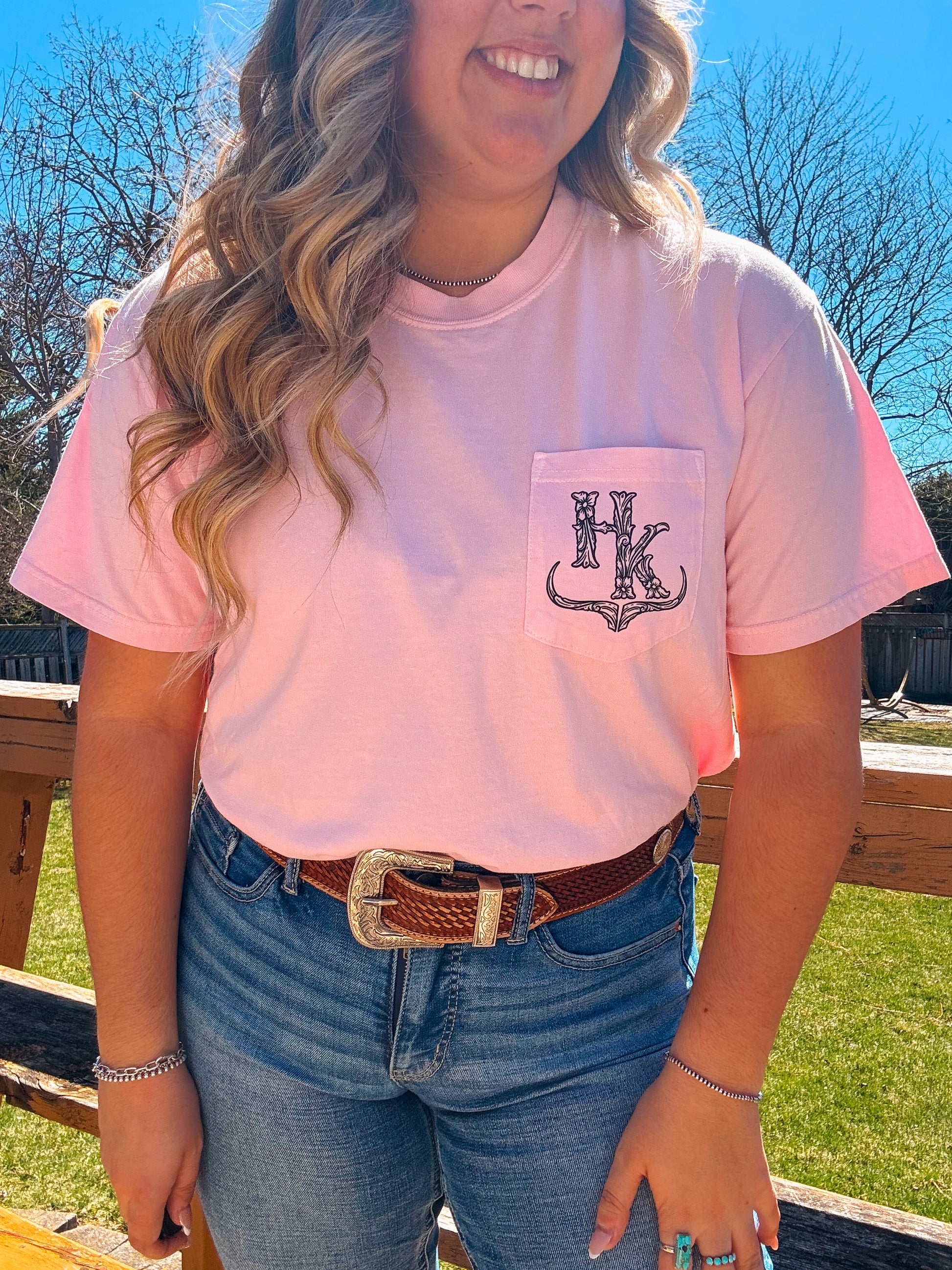 Modeled image of the Blossom Pink branded pocket tee styled with denim jeans and western accessories, highlighting the logo placement.