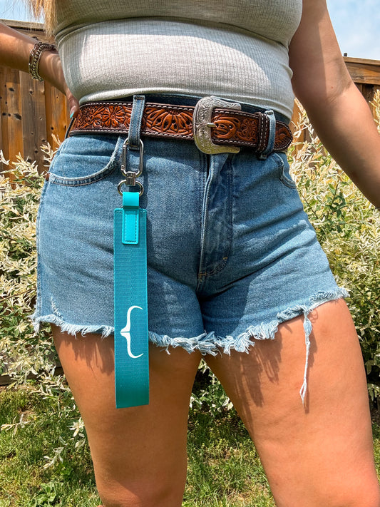 Turquoise blue wristlet with white HK bracket logo – clipped to belt loop, styled with tooled western belt.