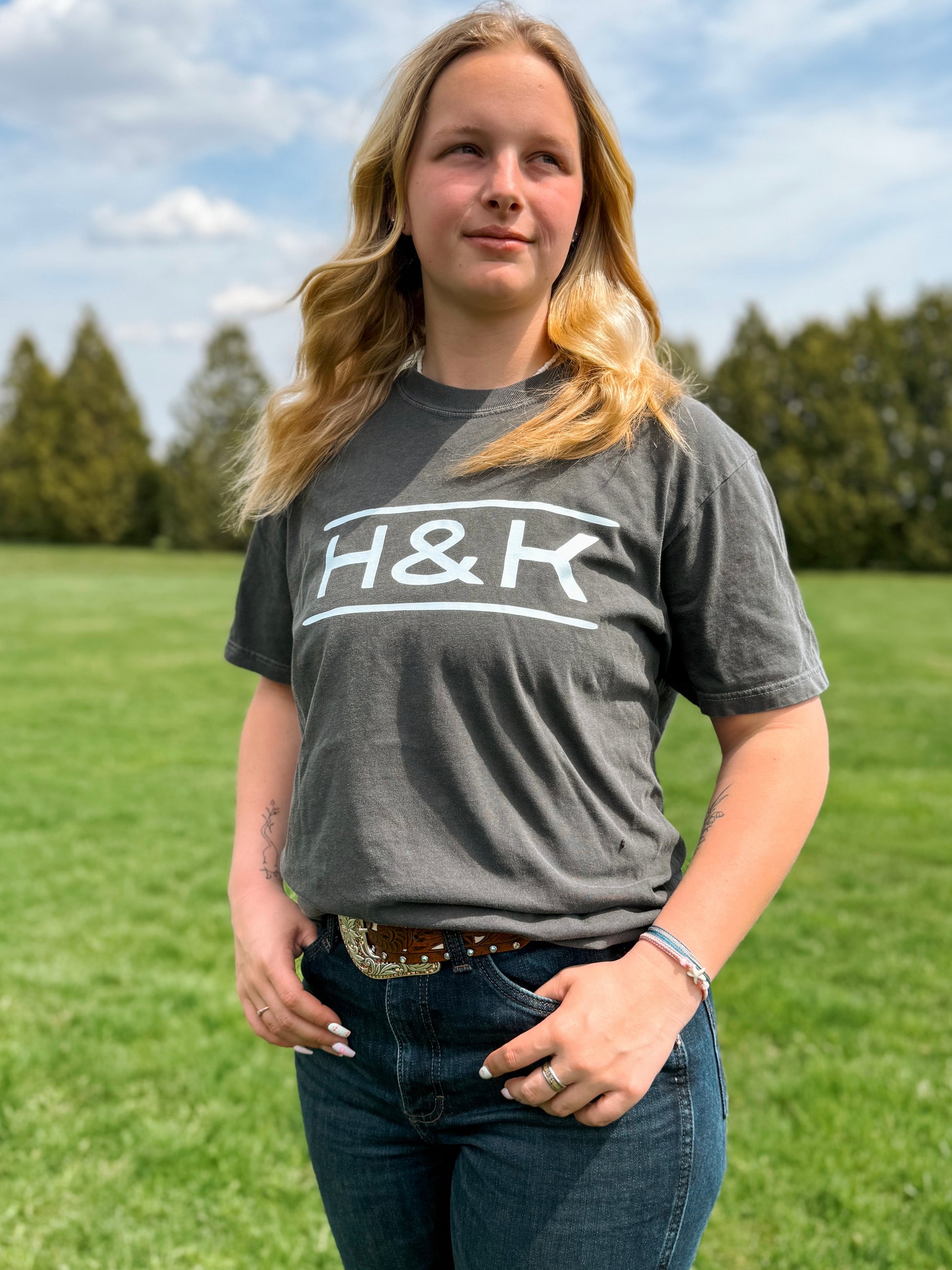 Full view of H&K branded tee in pepper styled with denim and a belt buckle