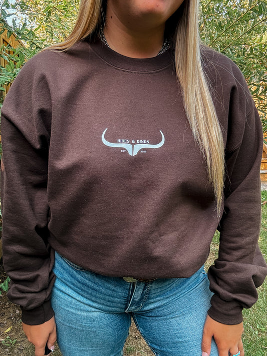 Close up view of Hides & Kinds Original Logo Crewneck in chocolate brown, featuring white steer head graphic and casual fit.