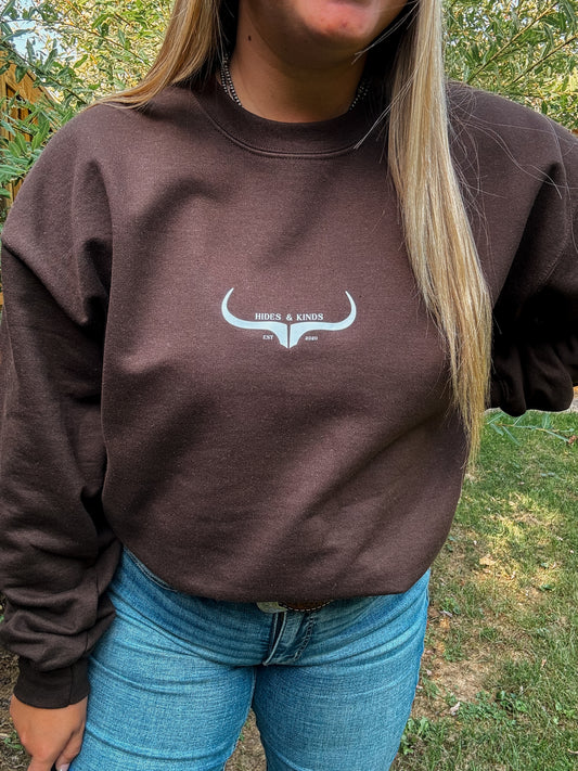 Outdoor photo of Hides & Kinds chocolate brown crewneck sweatshirt with original logo and relaxed styling.