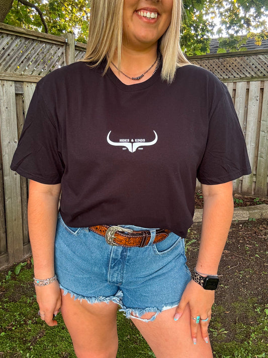 Close up of woman wearing black Hides and Kinds original logo tee styled with denim shorts, turquoise rings, and a western belt