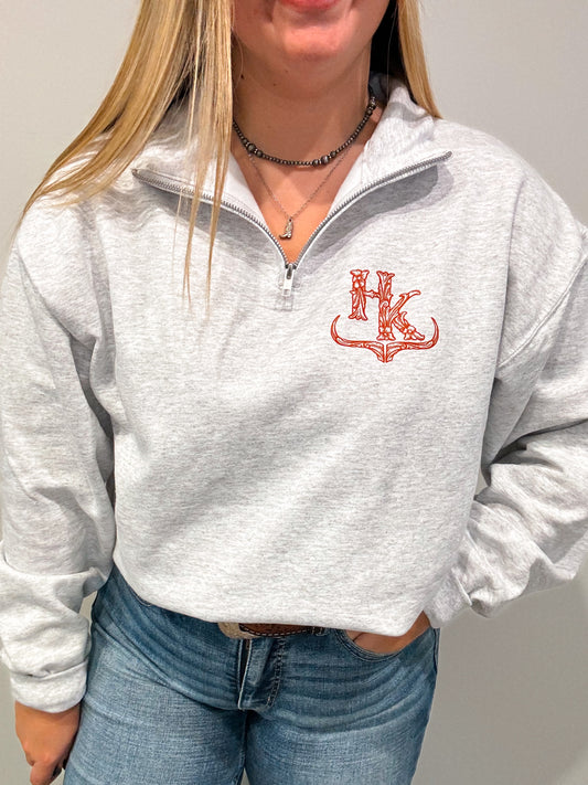 Front view of the Hides and Kinds quarter zip featuring a red western-style HK logo on ash grey fabric, styled with denim.