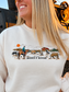 Close-up of the Homestead Crewneck graphic showing a cowboy on horseback, grazing cattle, a red barn and Hides & Kinds branding on cream fabric.