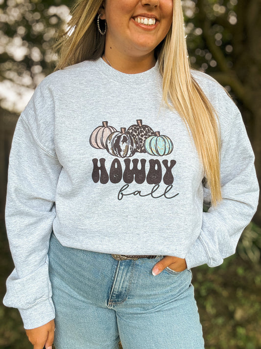 Close up of western fall crewneck with cowprint and leopard print pumpkins reading “Howdy Fall,” worn casually outdoors