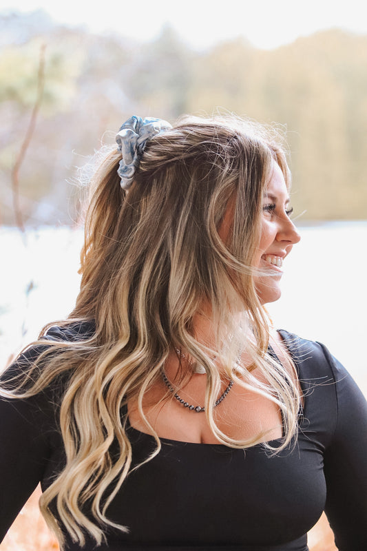 Model smiling while wearing light blue cowboy scene scrunchie in ponytail