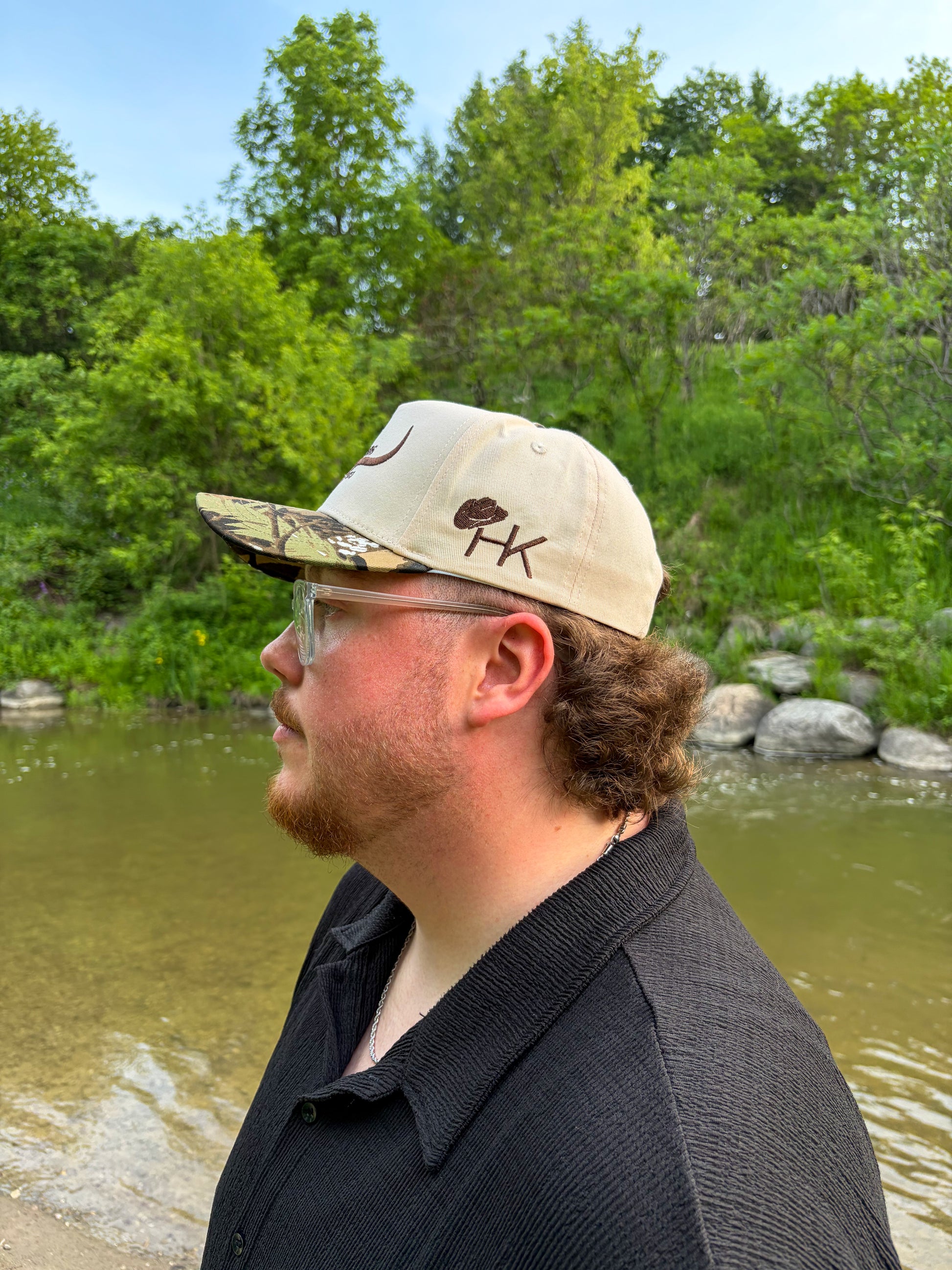 Side view of the Hides & Kinds Original Logo Hat (Camo) showing the embroidered HK logo and structured snapback fit.