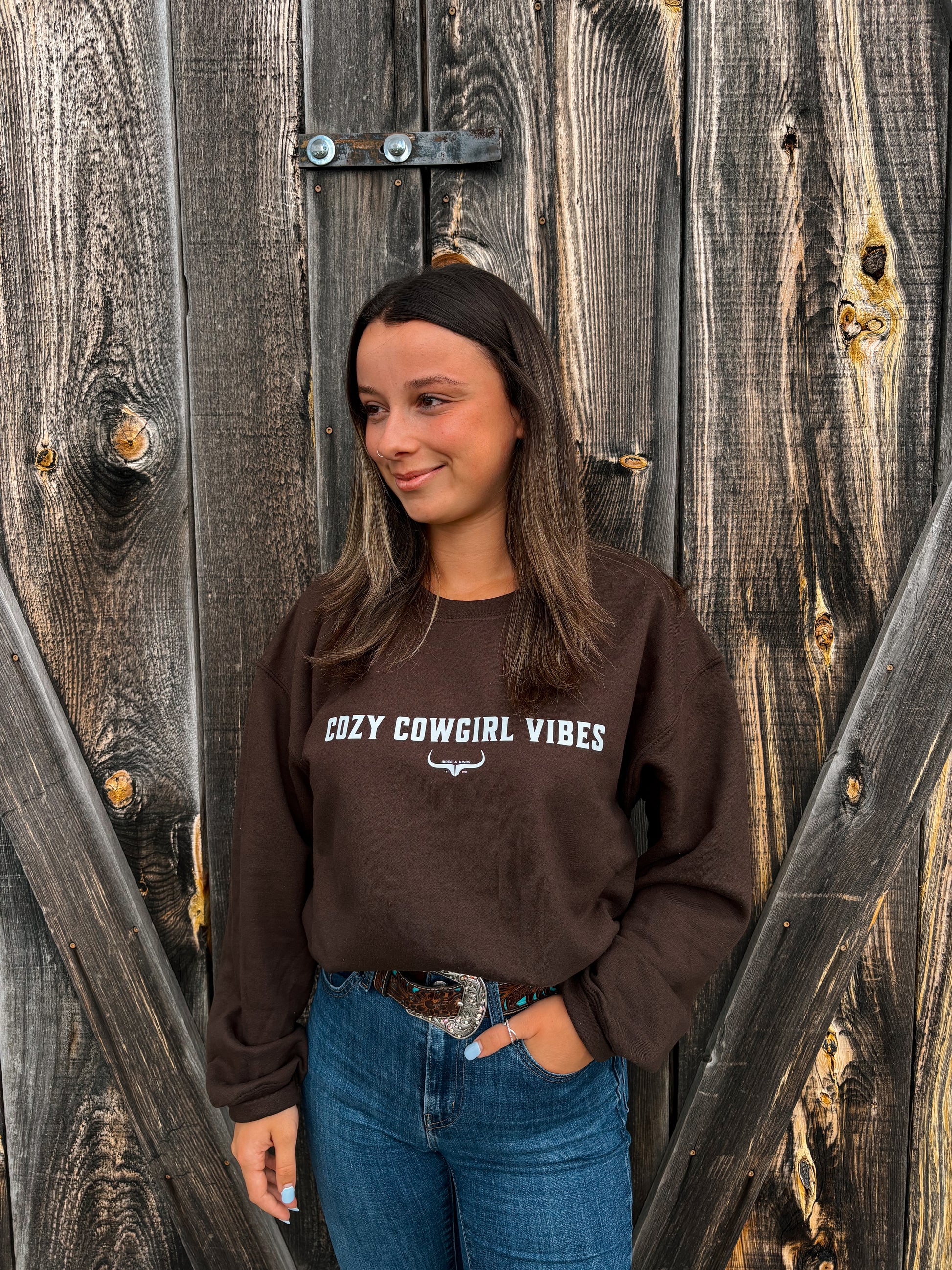 Model smiling while wearing the Cozy Cowgirl Vibes Crewneck from Hides & Kinds in chocolate brown