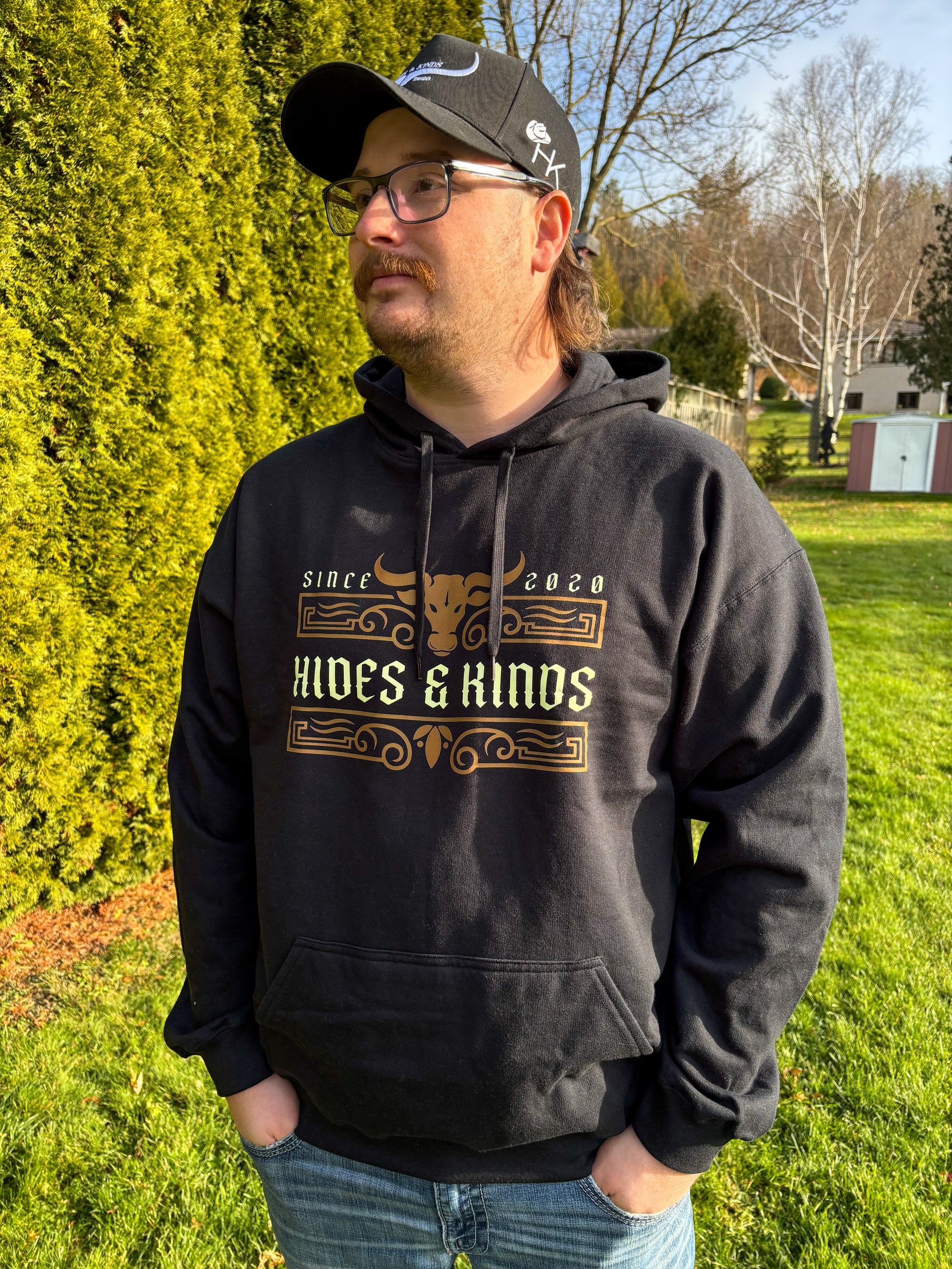 Lifestyle photo of men’s black Ranchline hoodie featuring gold Hides & Kinds western design