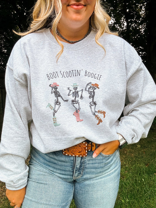 Close up of Skeleton Boot Scootin' Crewneck with three dancing skeletons in cowboy hats and boots, worn with light wash denim.