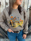 Close-up of the Hides & Kinds Stockman Crewneck in brown, showing a western ranch graphic with a cowboy on horseback, cattle, red barn and windmill.