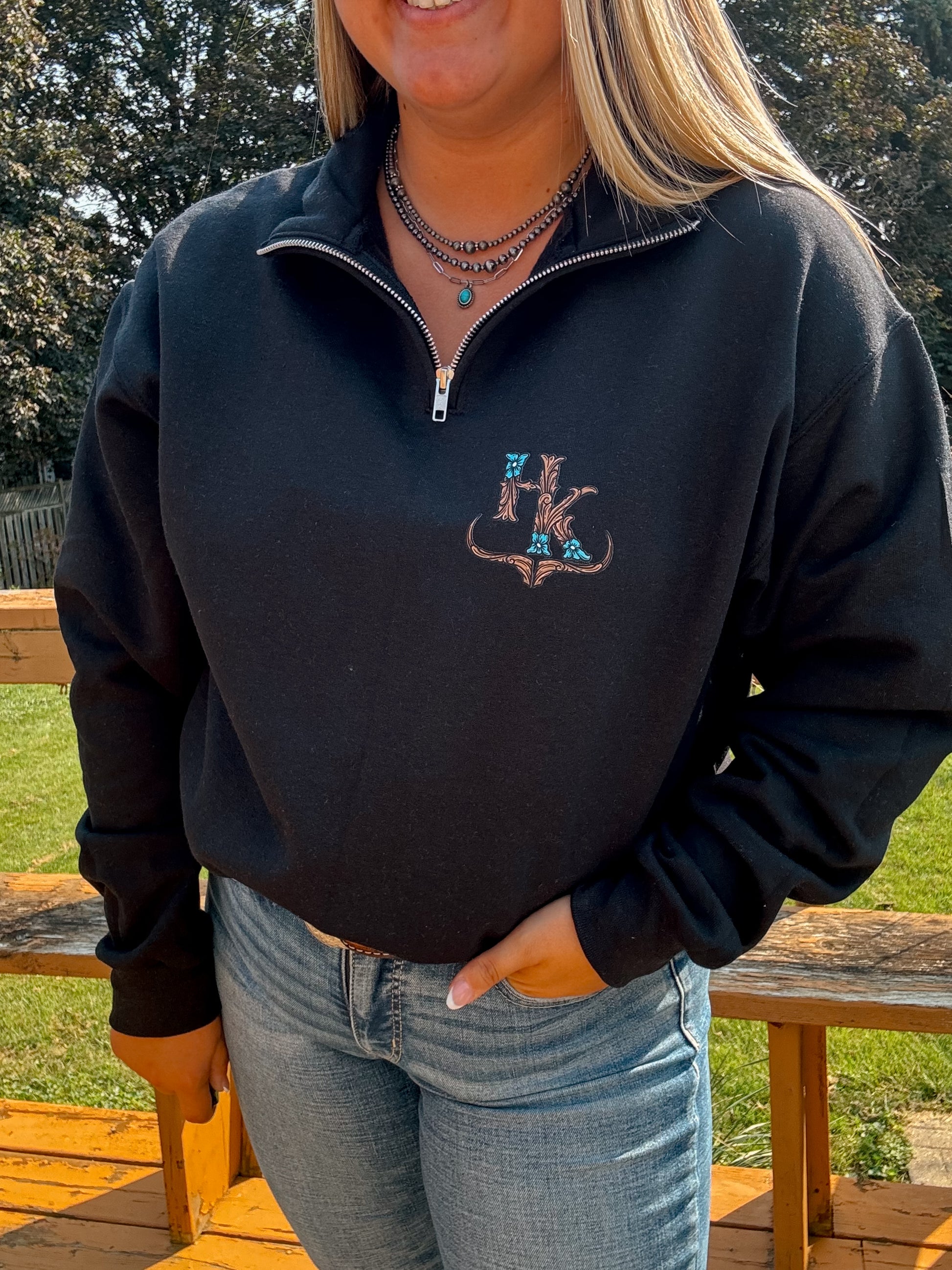 Close-up of the tooled turquoise logo embroidery on black quarter zip – textured western branding from Hides and Kinds.