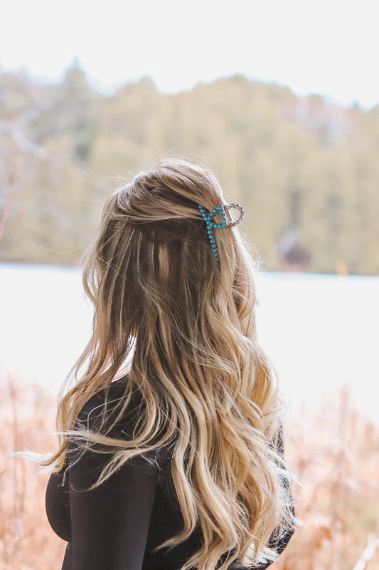 Back view of turquoise claw clip securing long blonde hair outdoors
