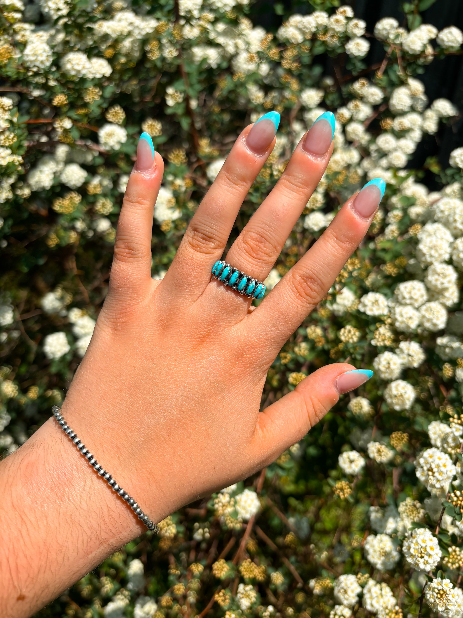 Hand wearing a sterling silver turquoise marquise ring against white flower background