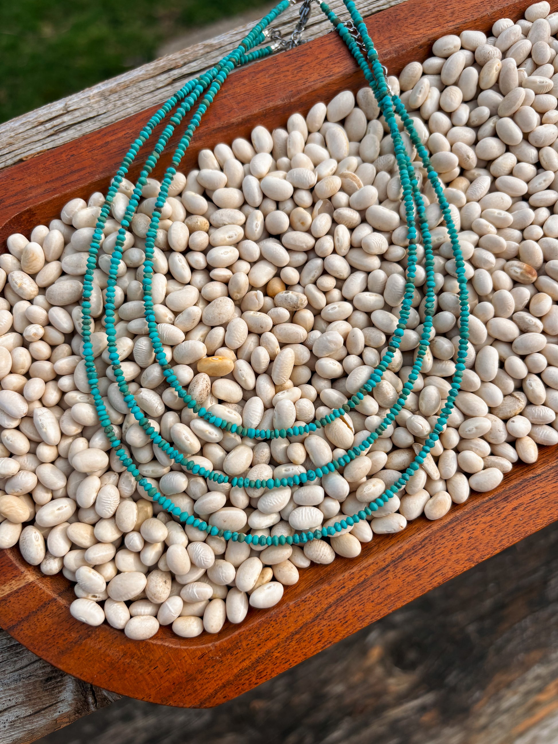 Flatlay of Turquoise Sierra Necklace displayed on a bed of white beans in a wooden tray.