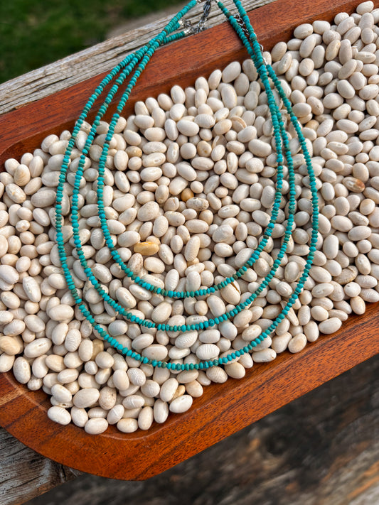 Flatlay of Turquoise Sierra Necklace displayed on a bed of white beans in a wooden tray.