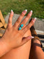 Close up of a hand wearing the Twin Trails Ring with two teardrop turquoise stones set in sterling silver.