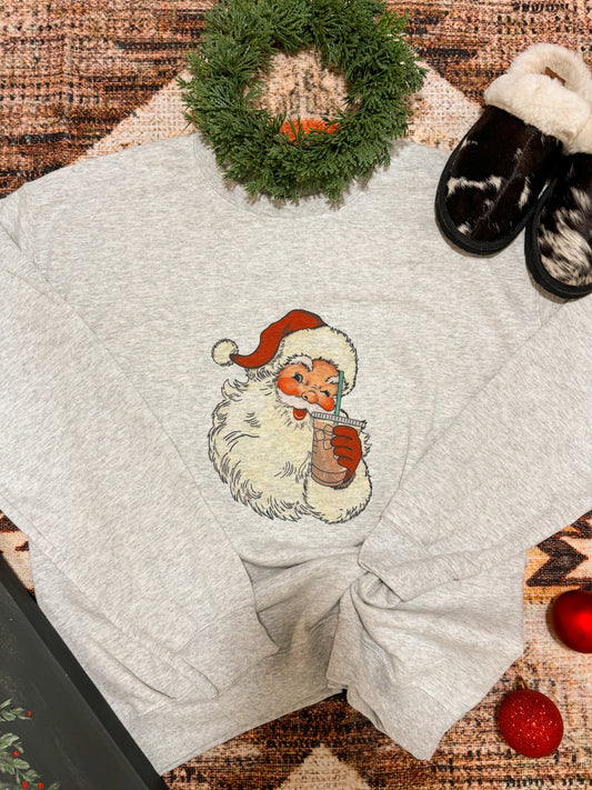 Flat lay of the Vintage Santa crewneck with iced coffee graphic on heather grey, styled with holiday decor